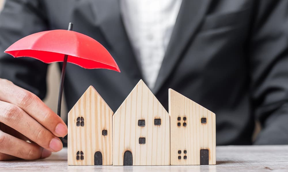 A tiny model house being protected by a cute red umbrella that symbolizes first-time home insurance
