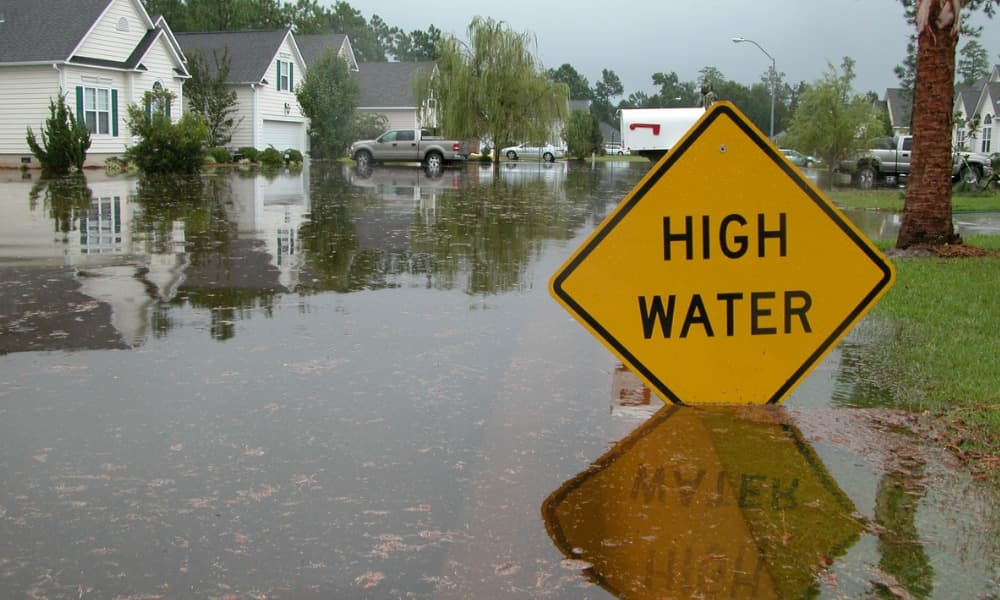 A flooded residential street with a “high water” sign.