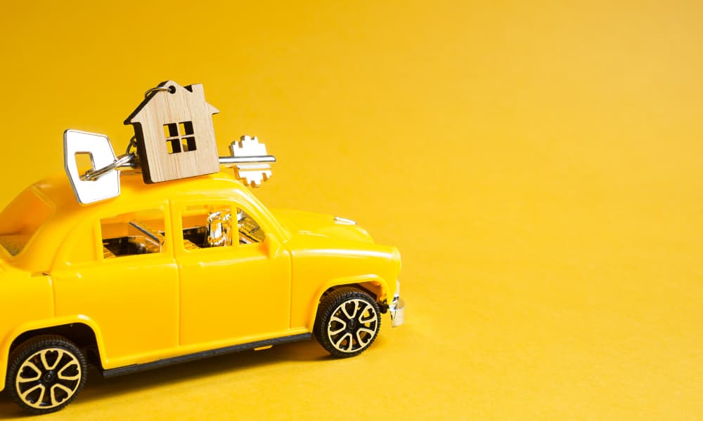 A yellow toy car with a house key on the roof against a yellow background.
