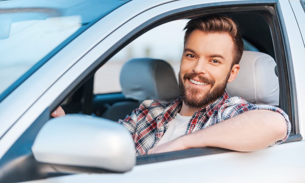 A smiling New York driver at the wheel of his stationary car.
