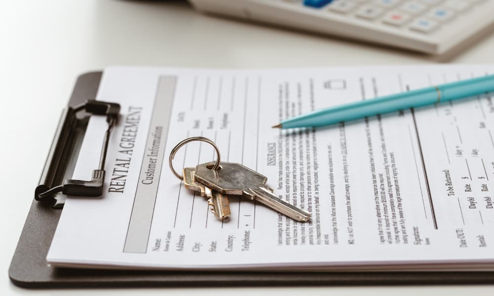 Paperwork for a New York rental agreement attached to a clipboard arranged with keys, a pen, and a calculator.
