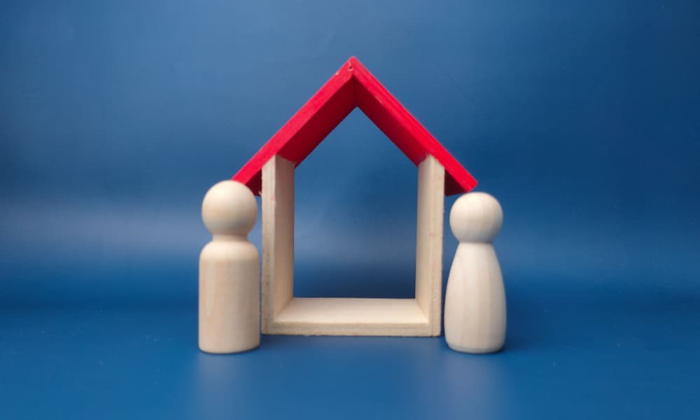 Two simple wooden figures beside a model home against a blue background.